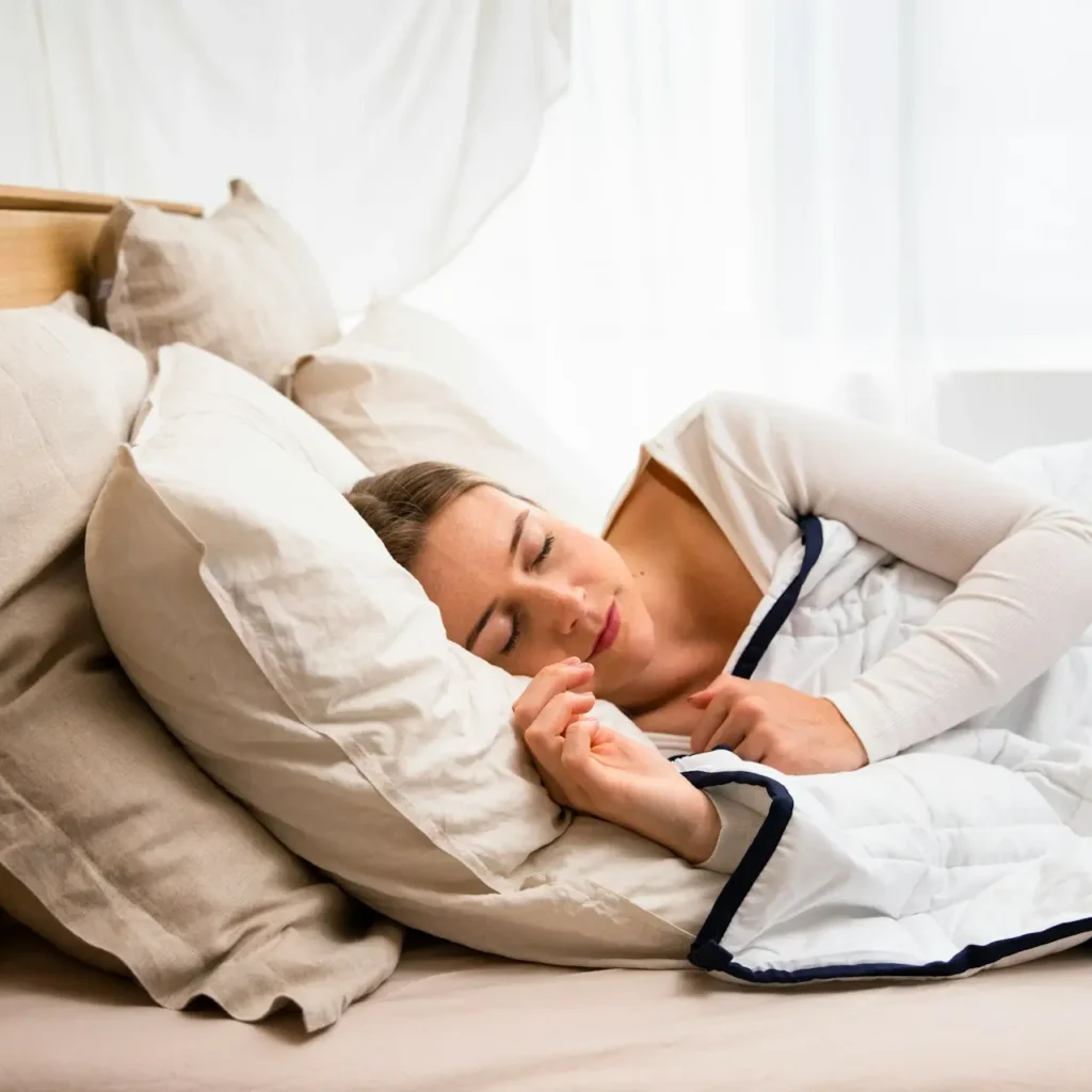 Femme sereine endormie dans une chambre à coucher plongée dans l'obscurité, illustrant les bonnes habitudes pour un sommeil réparateur.