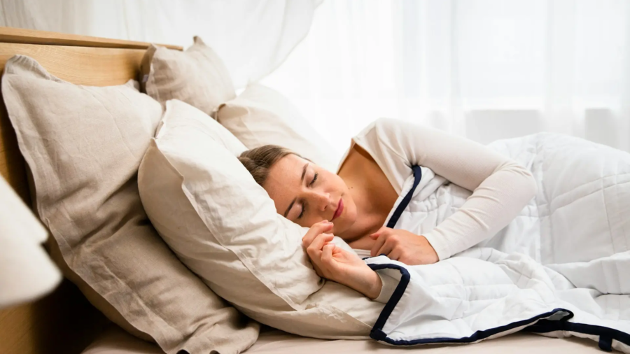 Femme sereine endormie dans une chambre à coucher plongée dans l'obscurité, illustrant les bonnes habitudes pour un sommeil réparateur.